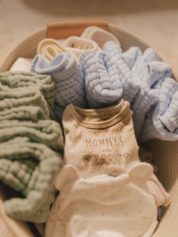 A basket of folded muslin baby clothes and a onesie