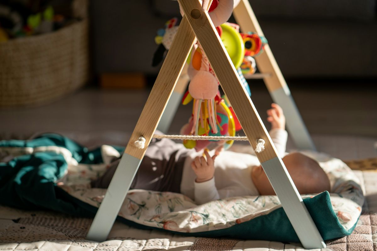A baby reaching up at a wooden activity play gym