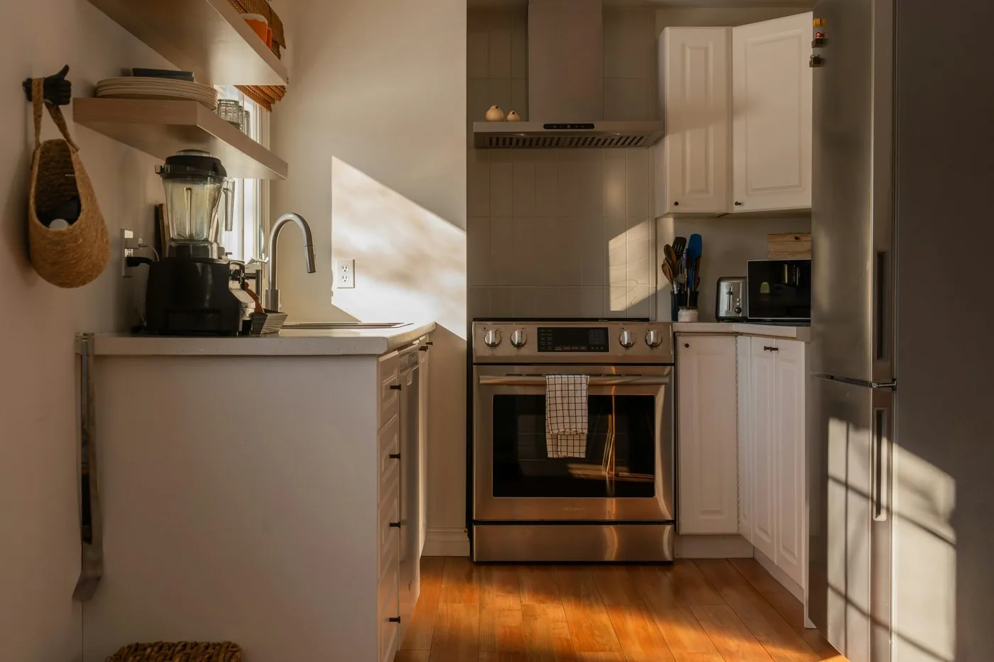 A sunlit kitchen with open shelving, a stainless range, and warm morning light on wood floors