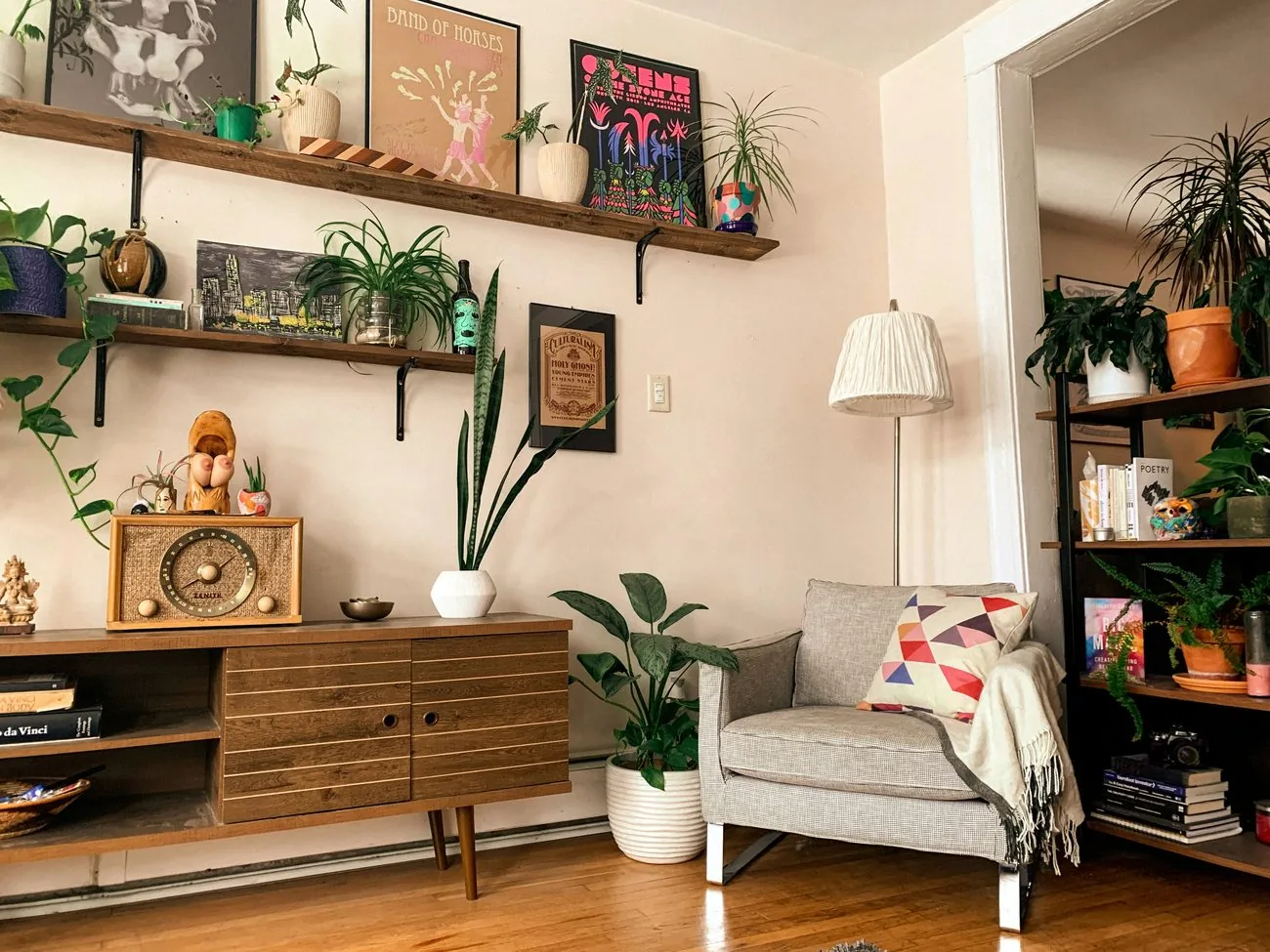 A cozy living-room corner with a lamp, a soft throw over an armchair, plants, and a mid-century sideboard
